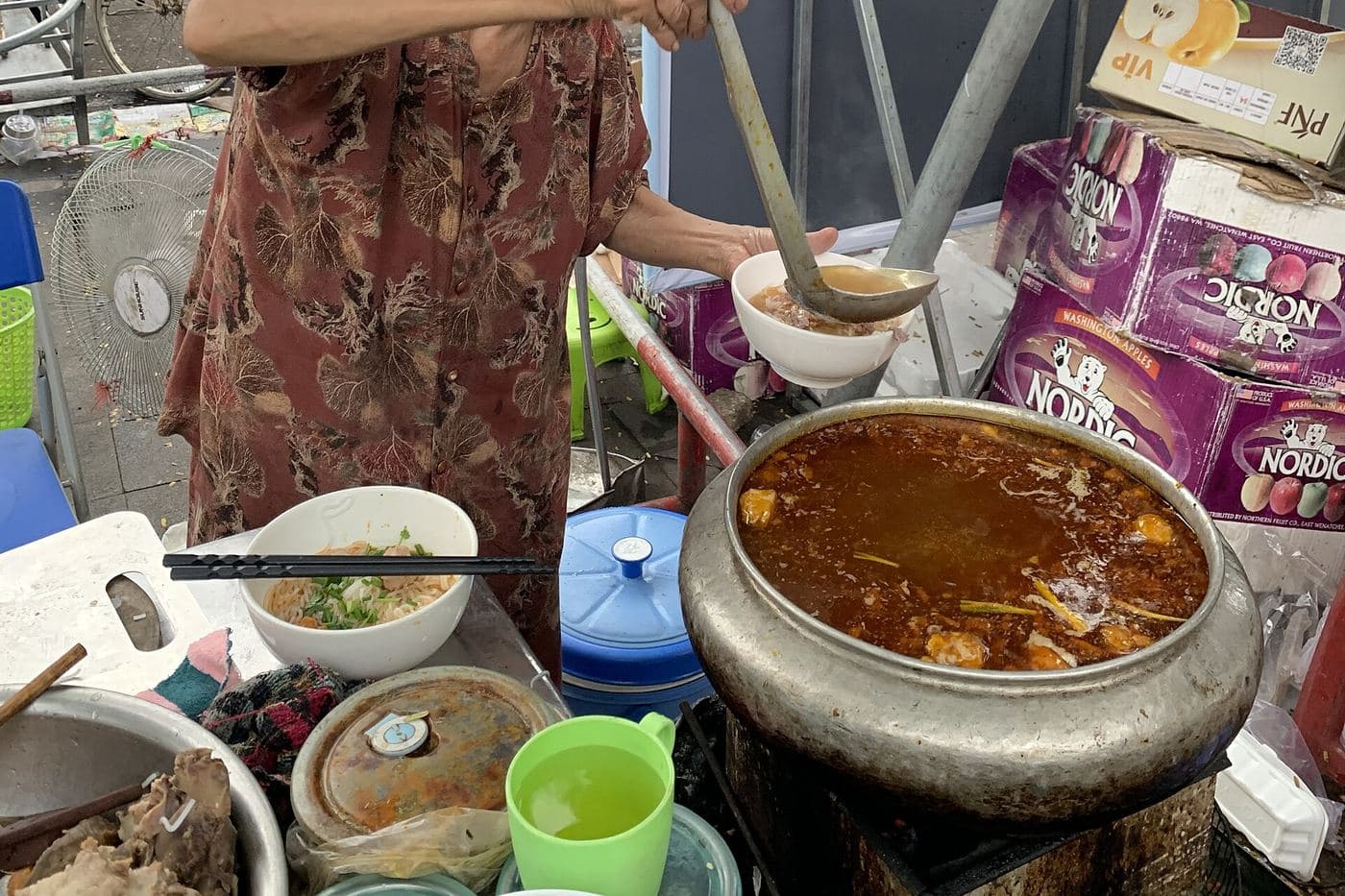 Уличная торговка разливает bún bò Huế из большого котла