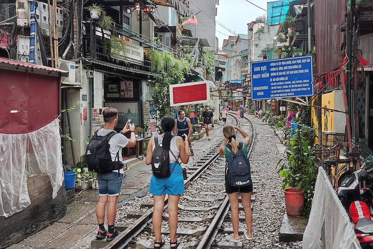 Туристы снимают на телефоны на Train Street в Ханое, у таблички с запретом съёмки