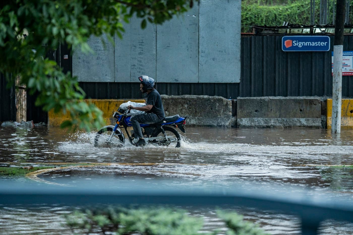 Мотоциклист в шлеме едет по затопленной паводком городской улице